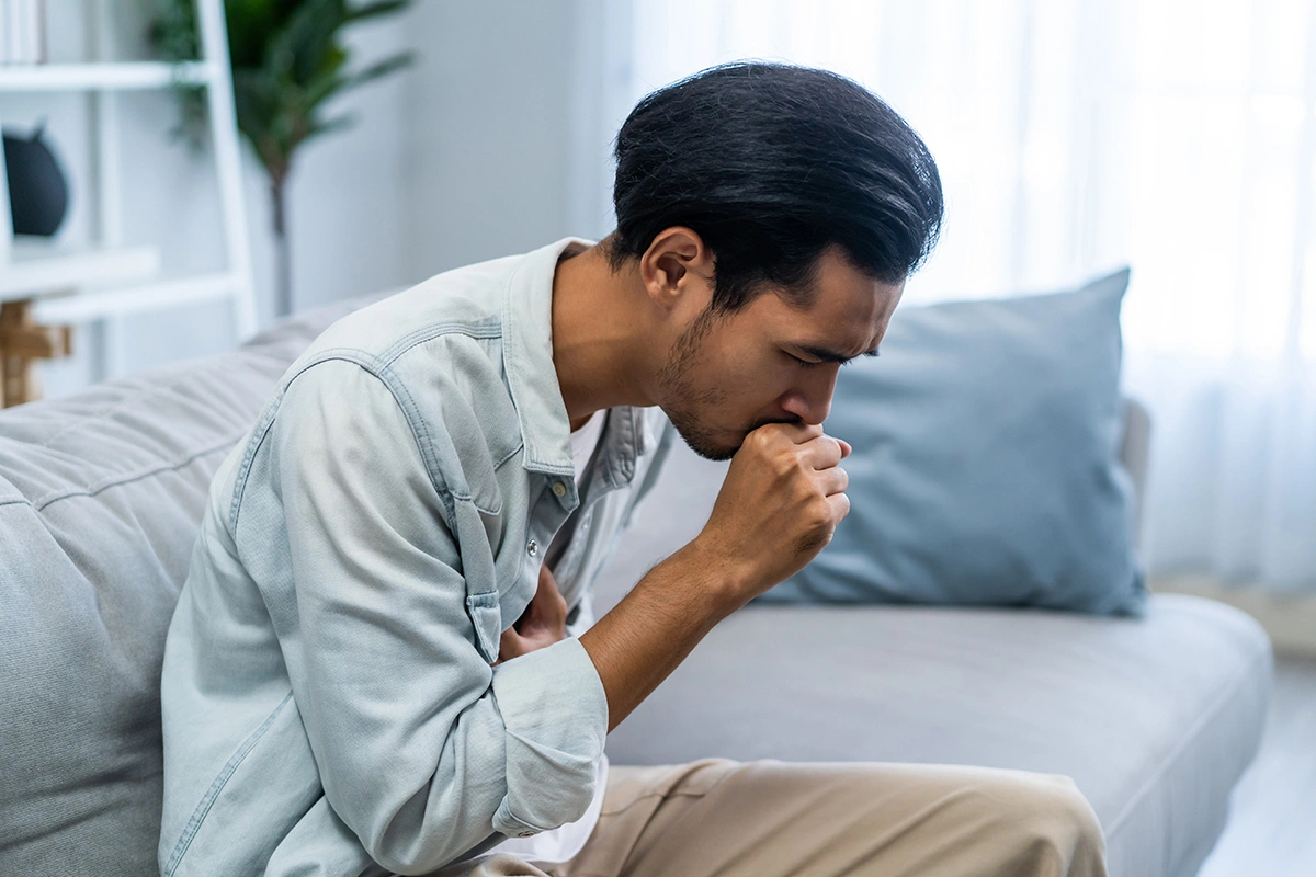 Man coughing while holding his lower abdomen due to increased abdominal pressure. 
