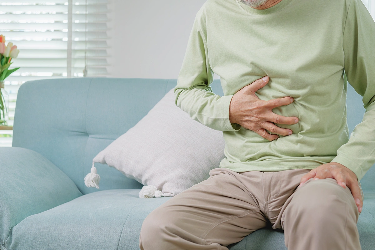 Elderly man holding the area of a previous abdominal hernia surgery scar while experiencing discomfort.